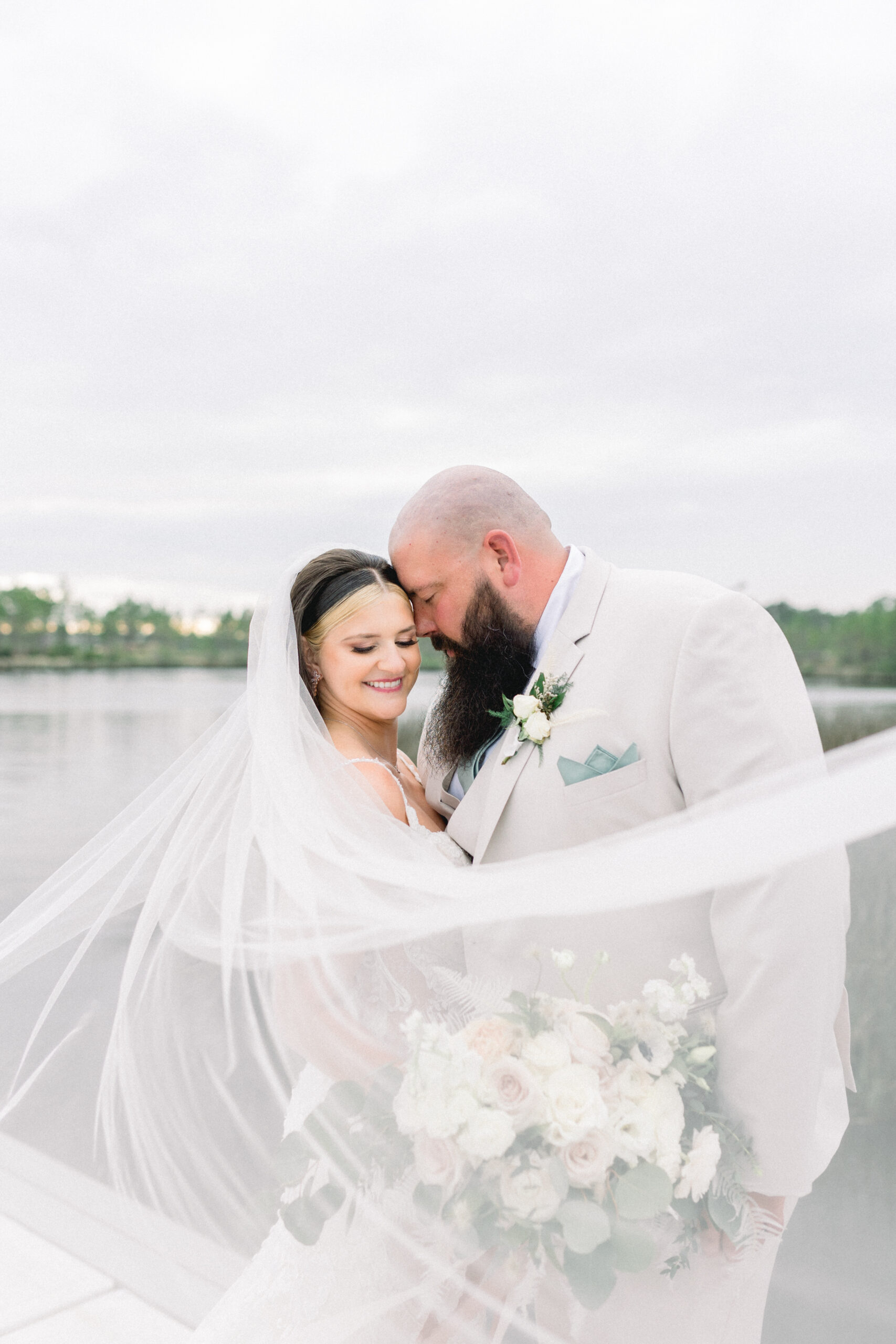 bride and groom with veil and flowers near water